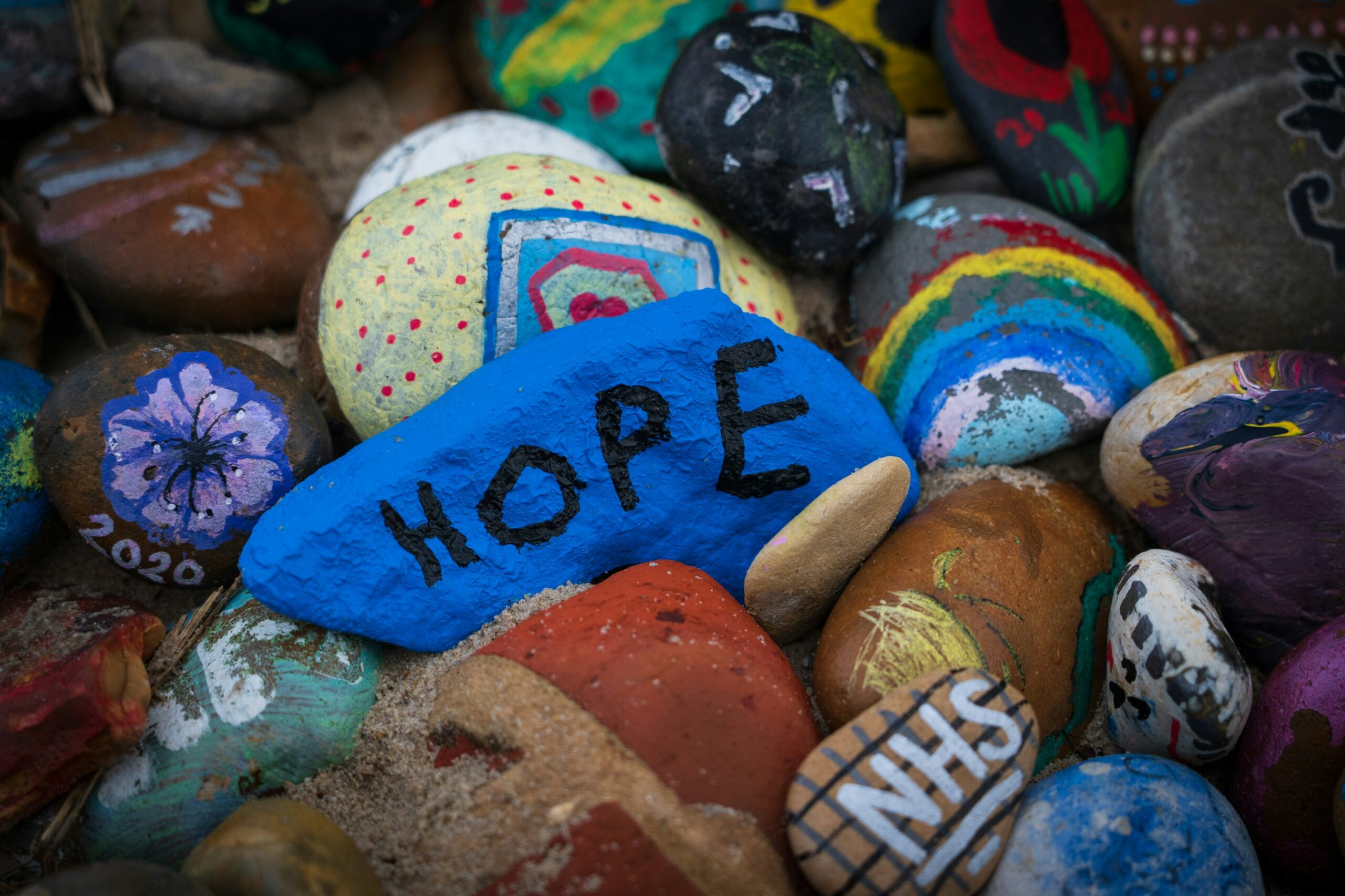 A collection of painted rocks. The middle one is navy blue and says "HOPE". Two other rocks on the sides say "NHS" and "2020".